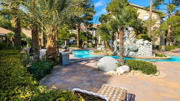 A resort pool area with palm trees, a stone waterfall, and lounge chairs.