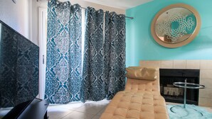 A modern bedroom with a sofa bed, patterned curtains, a round mirror, and a fireplace.