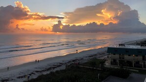 A beach view with a sunset, waves, and a building with a balcony overlooking the ocean. - Beautiful Direct Ocean Front View Condo (New Smyrna Beach)