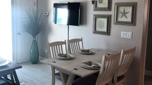 A dining area with a table and chairs, a flat-screen TV mounted on the wall, and a ceiling fan. - Beautiful Direct Ocean Front View Condo (New Smyrna Beach)