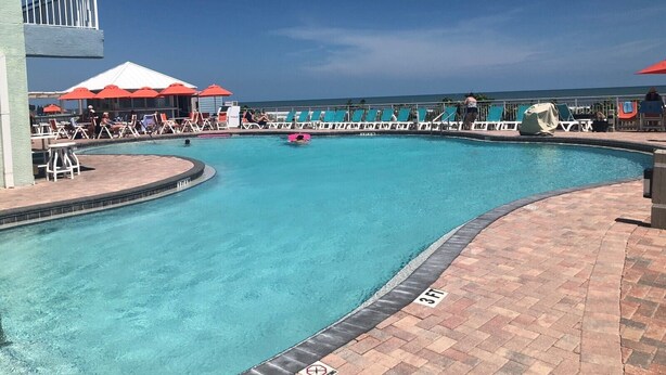 A pool area with lounge chairs, umbrellas, and a lifeguard stand. - Beautiful Direct Ocean Front View Condo (New Smyrna Beach)