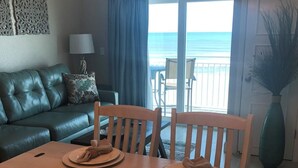 A dining area with a table set for two, a sofa, and a view of the ocean. - Beautiful Direct Ocean Front View Condo (New Smyrna Beach)
