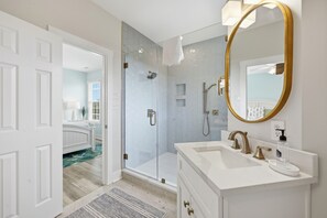 A modern bathroom with a glass shower enclosure, a white vanity with gold fixtures, and a large mirror with a gold frame. - Oceanside,private pool,golf cart,elevator,easy beach access,in Spinnaker's Reach (Emerald Isle)