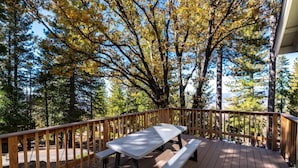 A wooden deck with a picnic table and benches, surrounded by tall trees with autumn foliage.