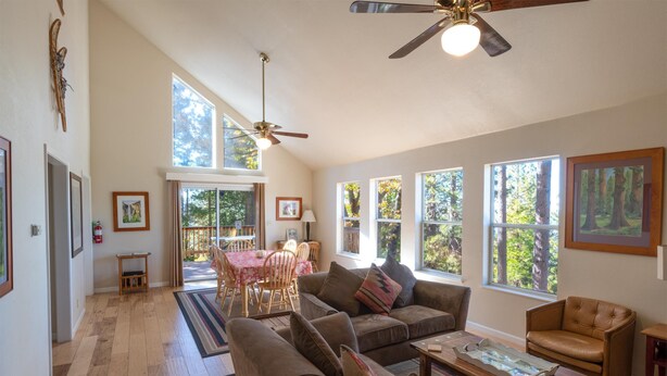 A spacious living room with a high ceiling, large windows, a ceiling fan, and a dining area with a table and chairs.