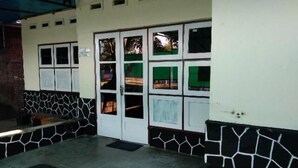 A room with a tiled floor, a bench, a door with glass panels, and a wall with a geometric pattern. - Olivia Homestay (Banyuwangi)