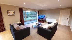 Una sala de estar con dos sofás negros, una mesa de centro, un televisor sobre un mueble bajo y un ventanal con cortinas.
