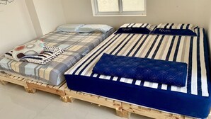 Zwei Betten mit unterschiedlicher Bettwäsche, ein Fenster mit gemusterten Vorhängen und eine Steckdose.