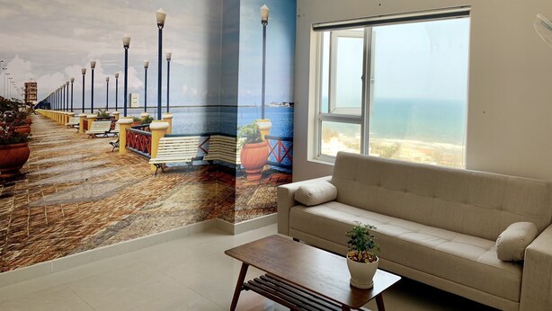Ein Zimmer mit einer großen Wandmalerei eines Küstenwegs, einem Sofa, einem Couchtisch und einem großen Fenster mit Meerblick.