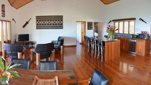 A spacious living area with a wooden floor, a dining table with chairs, a kitchen area with a microwave and sink, and a TV in the corner.