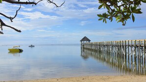 A beach with a wooden pier extending into calm waters, a small boat, and a thatched-roof structure.