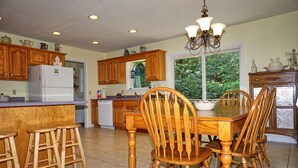 A kitchen with wooden cabinets, a white refrigerator, a dining table with chairs, and a chandelier. - Willow Tree Lodge-Easy access - Secluded - Grill (Bryson City)
