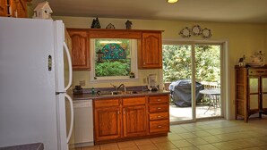 A kitchen with wooden cabinets, a refrigerator, a window with a view of greenery, and a sliding glass door leading to an outdoor patio. - Willow Tree Lodge-Easy access - Secluded - Grill (Bryson City)