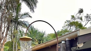 A private outdoor shower with a rain shower head, a small wooden stool, and a potted plant. - Beach Jungle: Pet-Friendly Hot Tub, Firepit & Pool in Beachside Hideaway (Byron Bay)