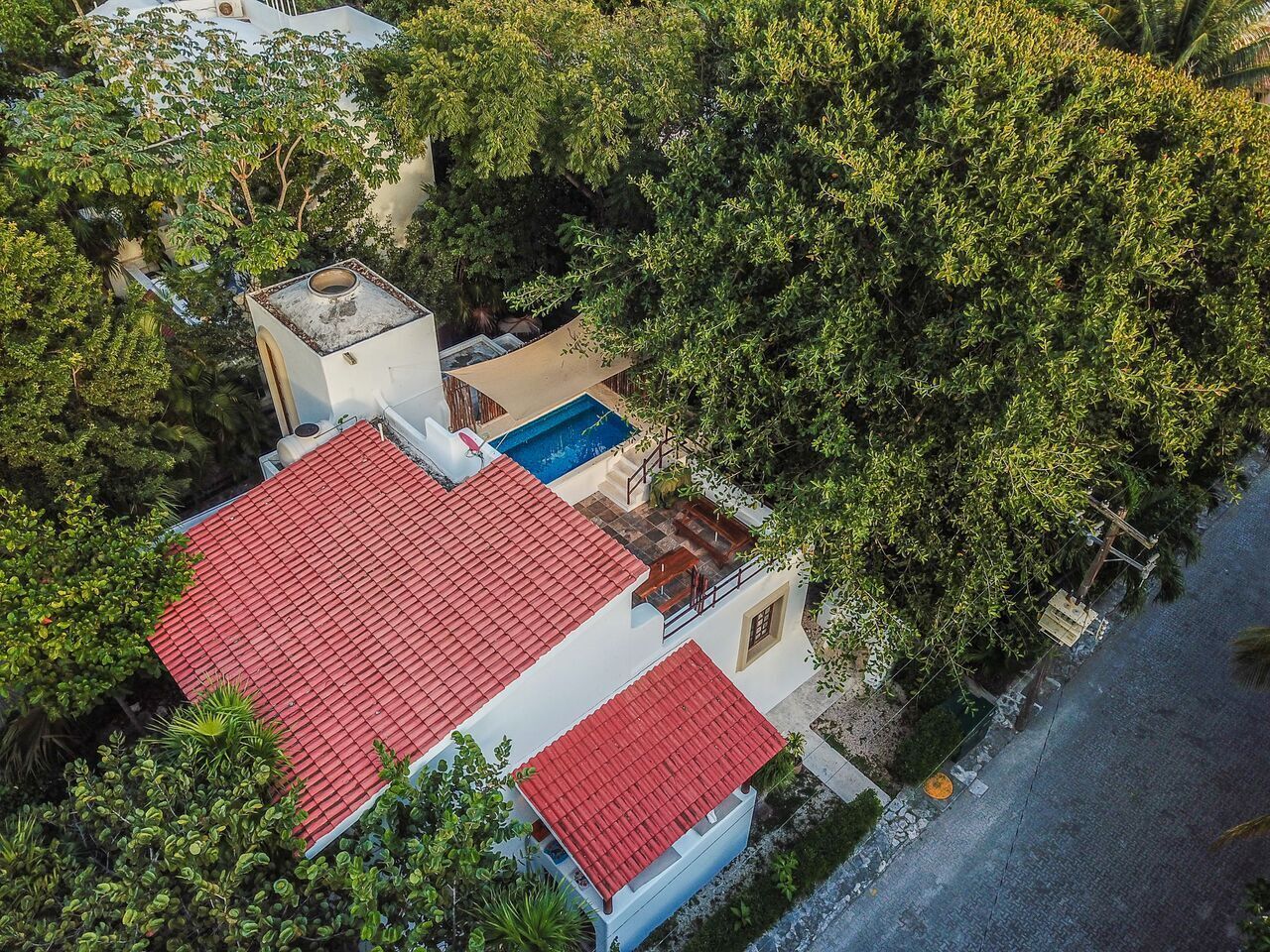 An aerial view of a house with a red-tiled roof, surrounded by dense greenery.