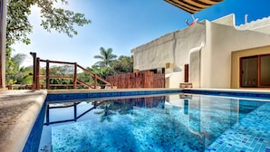 Una piscina azul cristalina con muelle de madera, rodeada por un edificio blanco con puerta roja y un ventanal grande.