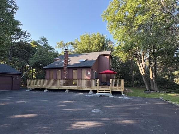 A two-story building with a wooden deck and a red umbrella. - Ash Cottage in Poconos near Camelback & Kalahari (Long Pond)