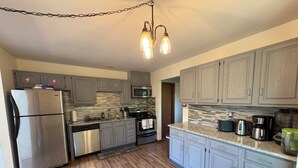 A kitchen with grey cabinets, stainless steel appliances, a wooden floor, and a hanging light fixture. - Ash Cottage in Poconos near Camelback & Kalahari (Long Pond)