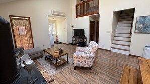 A spacious living room with a sofa, a patterned armchair, a wooden coffee table, and a TV. - Ash Cottage in Poconos near Camelback & Kalahari (Long Pond)