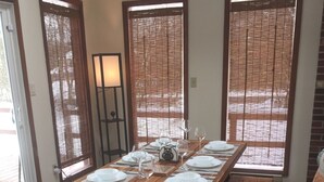 A dining area with a wooden table set for four, flanked by benches, and large windows with blinds. - Ash Cottage in Poconos near Camelback & Kalahari (Long Pond)
