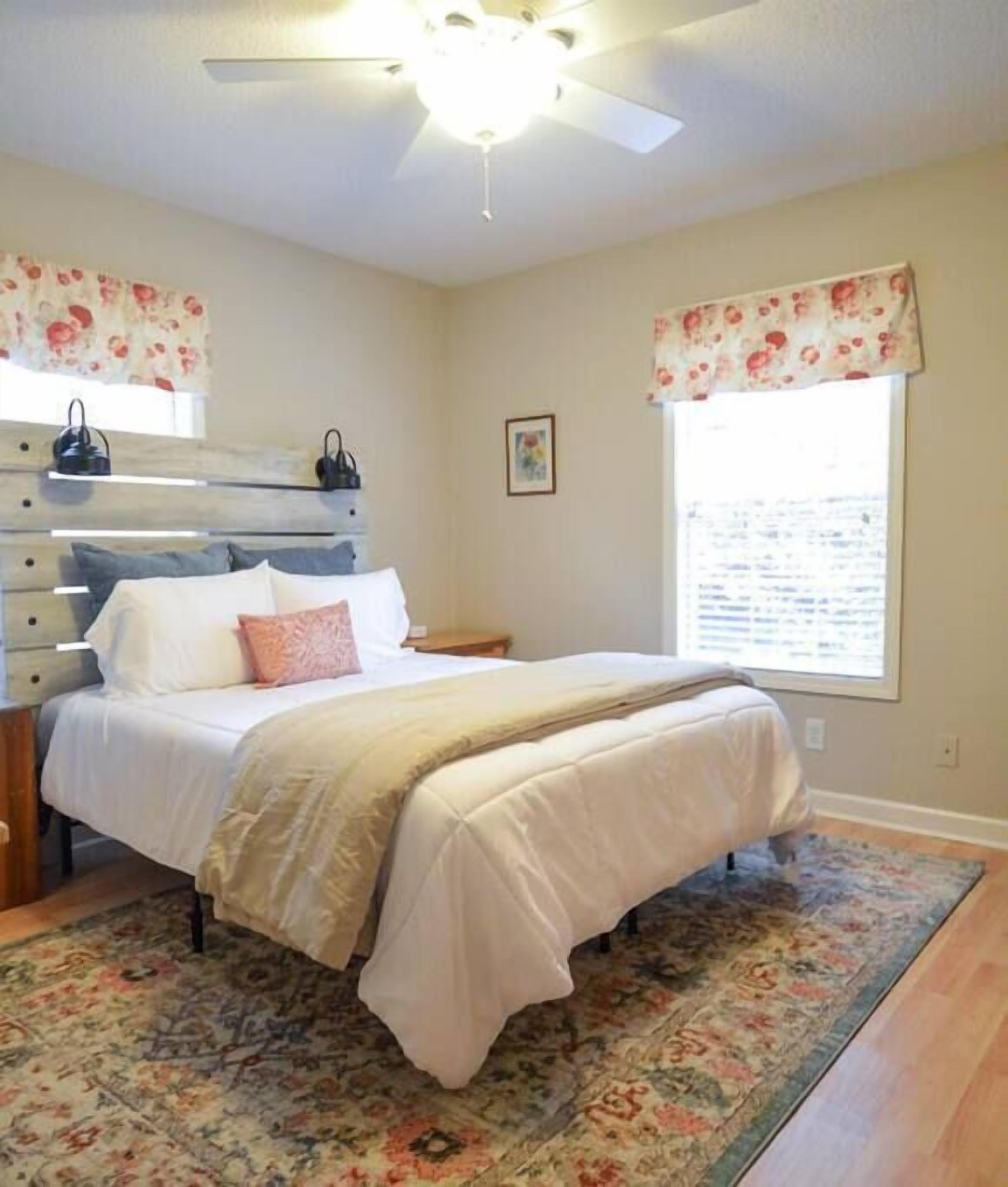 A bedroom with a bed, a ceiling fan, a window with curtains, and a floral rug.