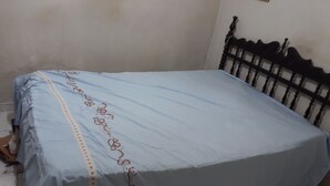 Ein Bett mit blauer Bettdecke und Blumenmuster, ein hölzernes Kopfende und eine kleine Holzablage.