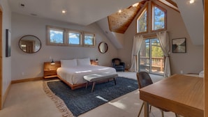 Ein Schlafzimmer mit einem großen Bett, einem Schreibtisch und einem Stuhl. Es gibt Fenster und eine Decke mit Holzbalken.