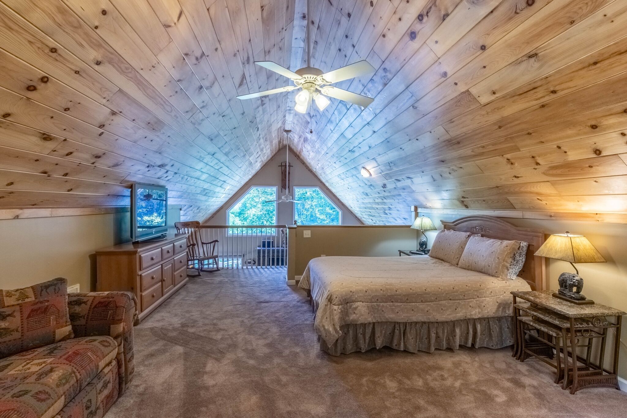A cozy attic bedroom with a sloped ceiling, a bed, a TV, a desk, and a chair.