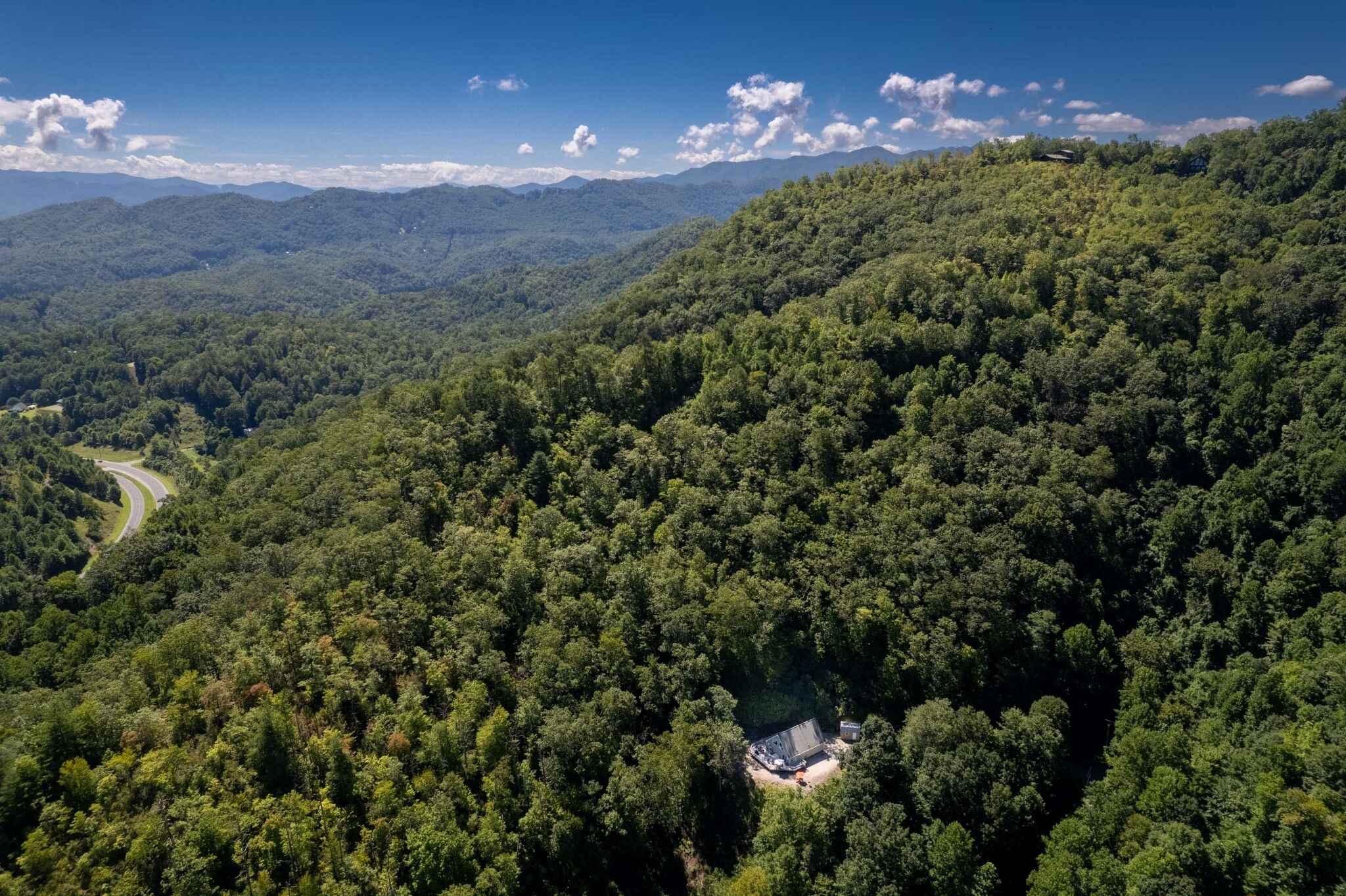 Une vue aérienne d’une zone boisée, avec une route sinueuse et un petit bâtiment entouré d’arbres denses.