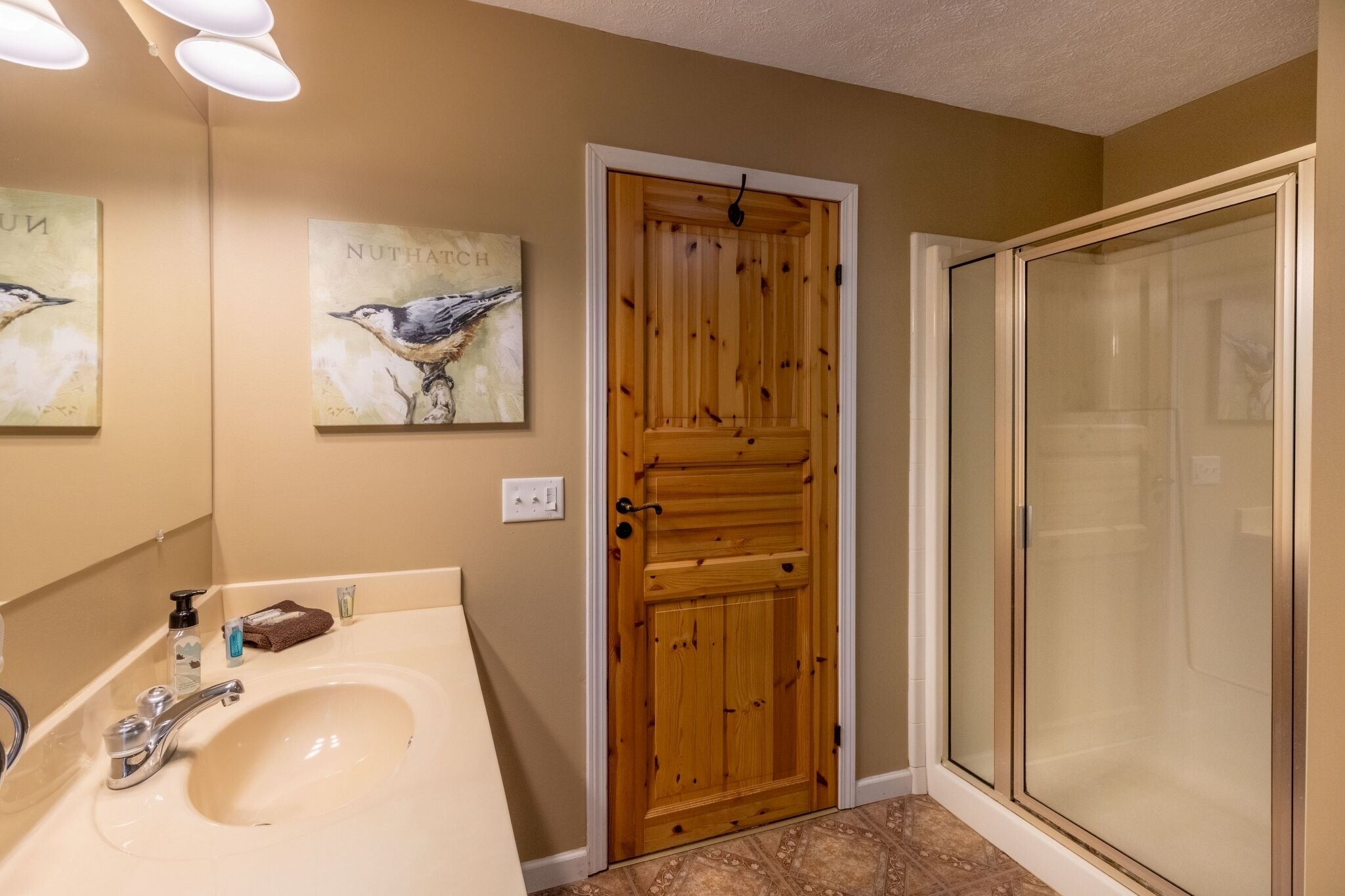 A bathroom with a wooden door, a sink with a mirror, and a shower area.
