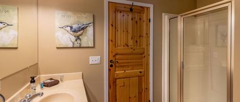 A bathroom with a wooden door, a sink with a mirror, and a shower area.
