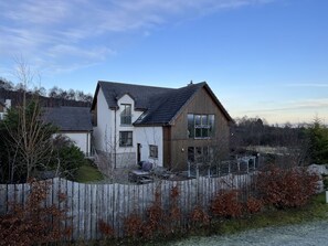 Une maison à deux étages, dotée d’un toit en pente, d’une clôture en bois et offrant une vue sur le paysage environnant.