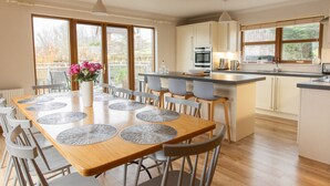Une cuisine moderne dotée d’un îlot central, de grandes fenêtres et d’un coin repas avec une table dressée pour six personnes.
