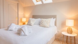 Une chambre d’hôtel avec un lit soigneusement fait, deux lampes de chevet, une table ronde avec une lampe et des fenêtres de toit.