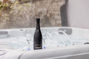 Une bouteille de champagne Freixenet et deux verres sur une table blanche dans un jacuzzi où l’eau coule.