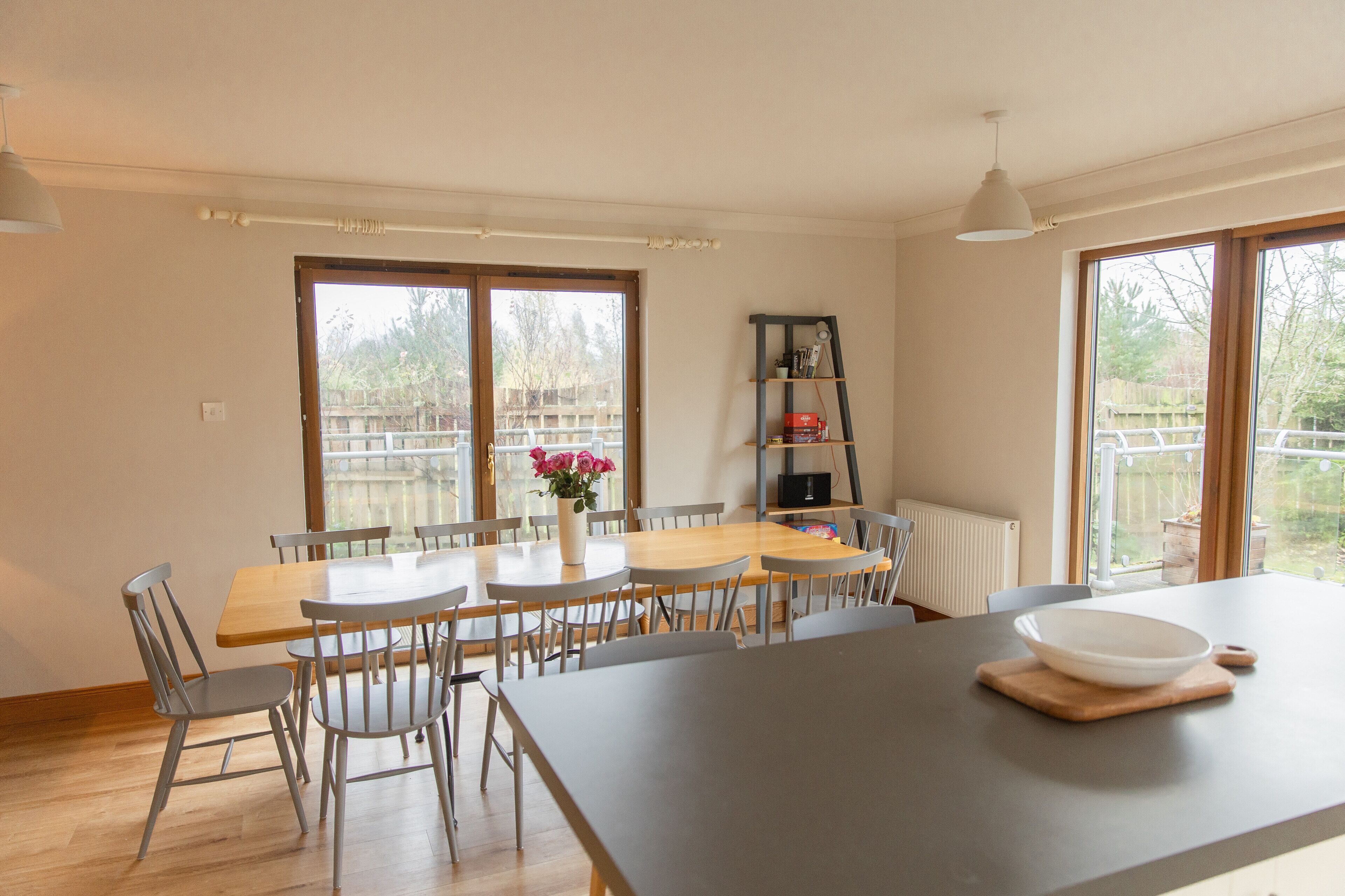 Un coin repas avec une table et des chaises en bois, un vase rempli de fleurs et une bibliothèque.