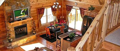 Een gezellig houten huisje interieur met een stenen open haard, een televisie, een eethoek en een trap.