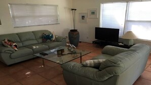 Een woonkamer met een groene bank, een glazen salontafel, een televisie en een lamp.