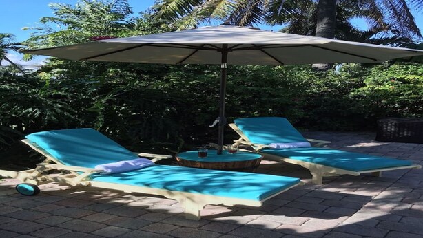 Twee ligbedden met een tafel en parasol in een tuin.