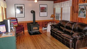 Una sala de estar acogedora con una chimenea de leña, un sofá de cuero, cuadros enmarcados en la pared y techo de madera.
