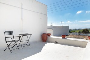 Eine Dachterrasse mit Metallstuhl und Tisch, Terrakottatöpfen und Blick auf die Landschaft.