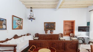 A traditional room with a wooden bed, a dining table with chairs, a wooden cabinet, a television, and artwork on the walls. - Marouso Villa Paros (Paros)