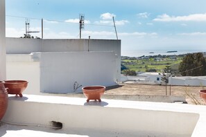 Eine Dachterrasse mit Terrakottatöpfen, einer weißen Mauer und Blick auf eine Küstenstadt.