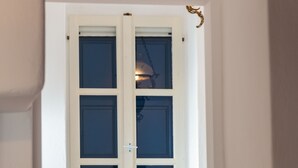 A narrow hallway with a white door, a window with blue shutters, a rustic wooden bench, and a large clay pot. - Marouso Villa Paros (Paros)