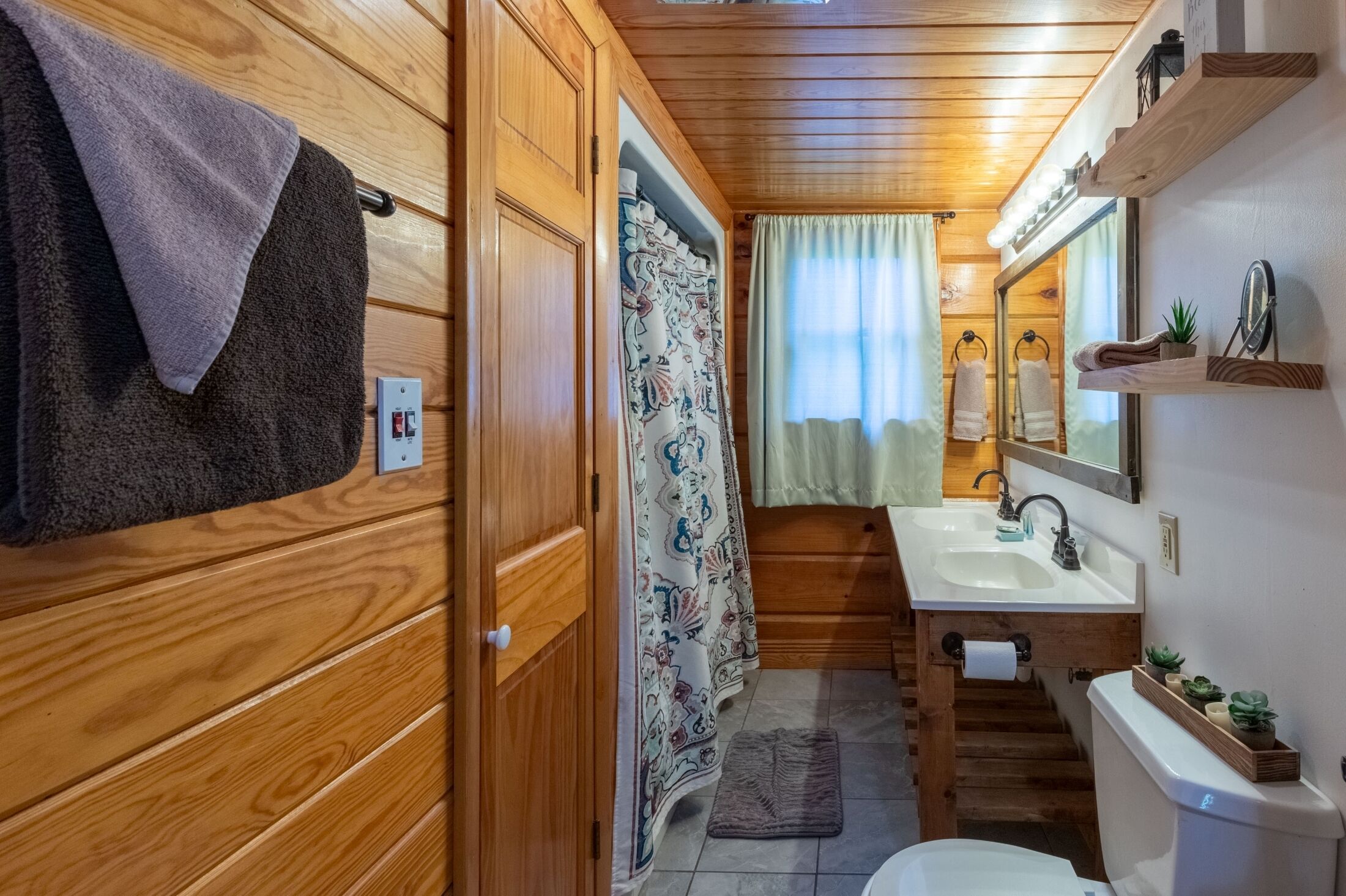 Een houten interieur met een badkamer, inclusief een wastafel, spiegel en handdoekhouder.