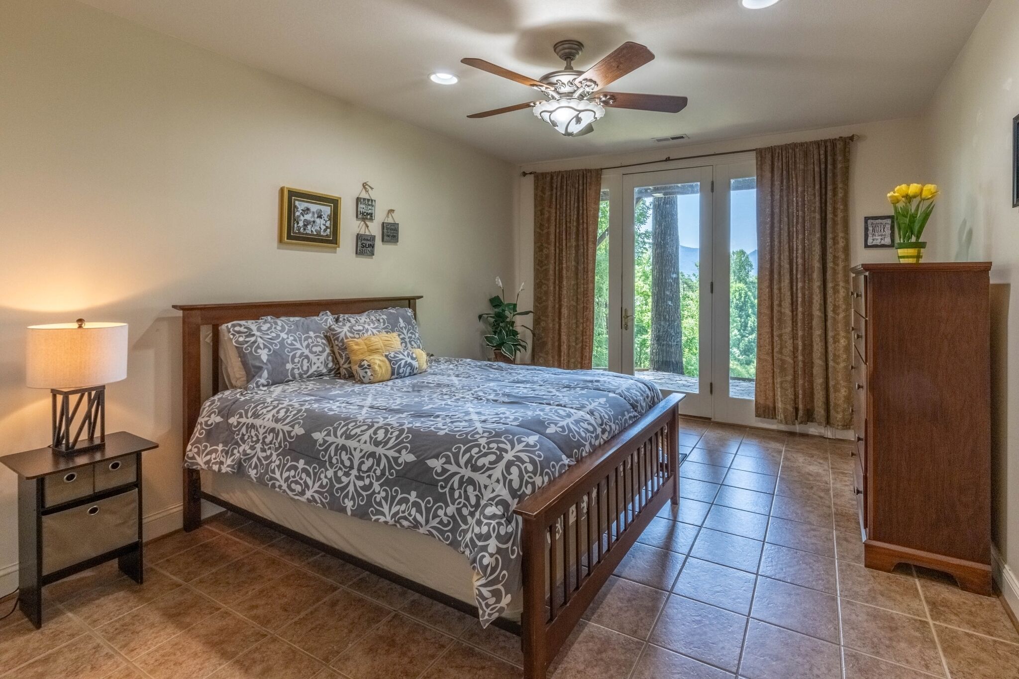 A bedroom with a bed, nightstand, ceiling fan, and a view of the outdoors through a sliding door.