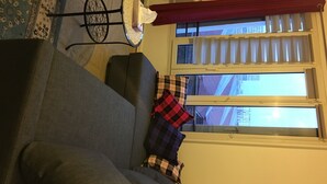 A living room with a grey sofa, a small round table, and a window with blinds. - Appartement of 2 rooms, bathroom, WC and kitchen all separate, take 5 persons (Créteil)