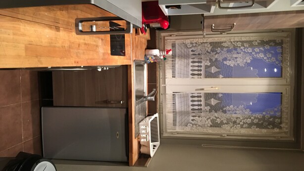 A compact kitchen with wooden cabinetry, a built-in oven, and a window with a floral pattern. - Appartement of 2 rooms, bathroom, WC and kitchen all separate, take 5 persons (Créteil)