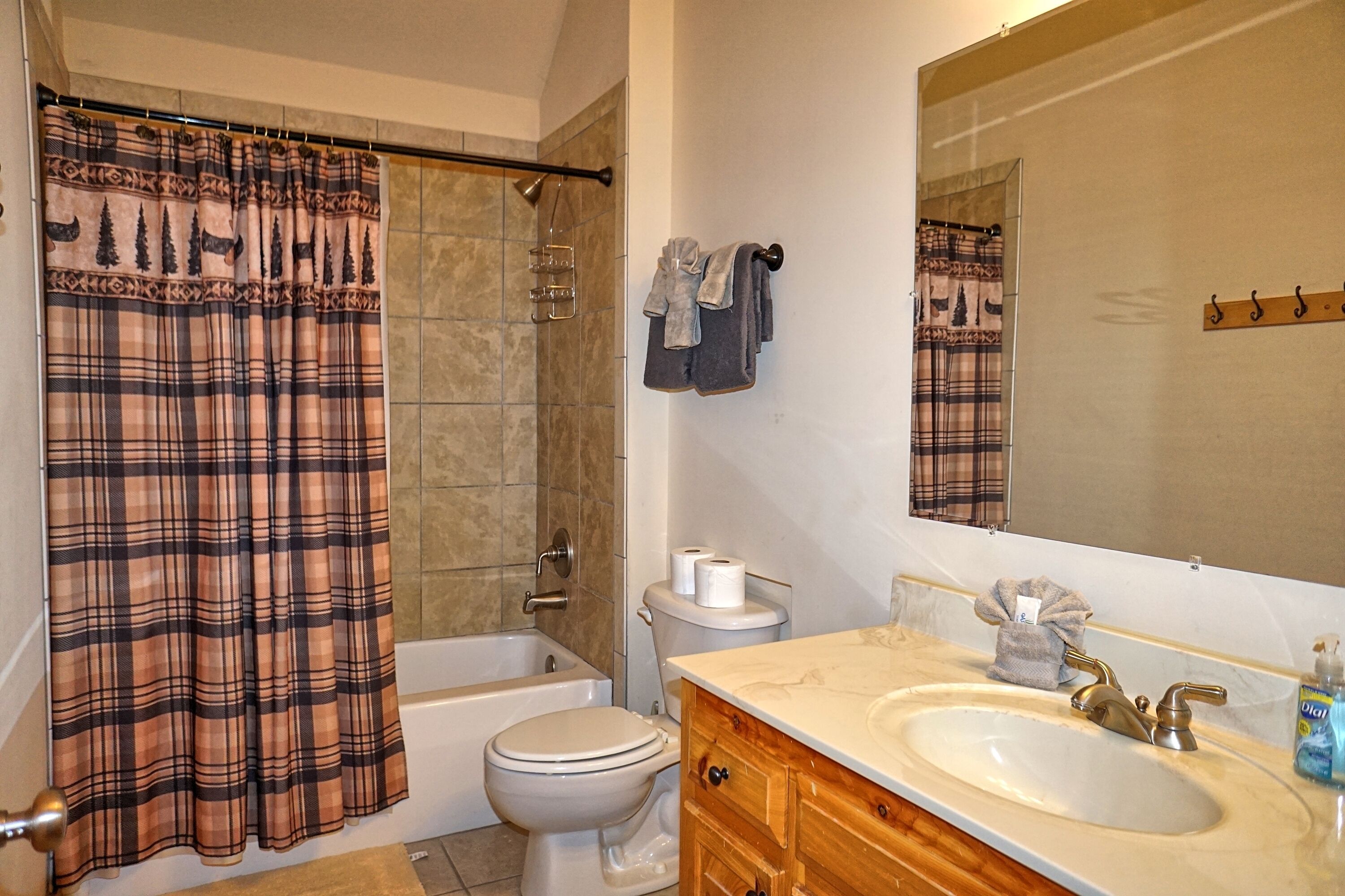 Un baño con cortina de ducha escocesa, un inodoro, una bañera, un lavabo y un espejo.
