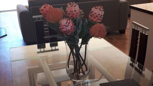 Un salon moderne avec une table basse en verre, un canapé et une table à manger agrémentée d’un vase de fleurs.